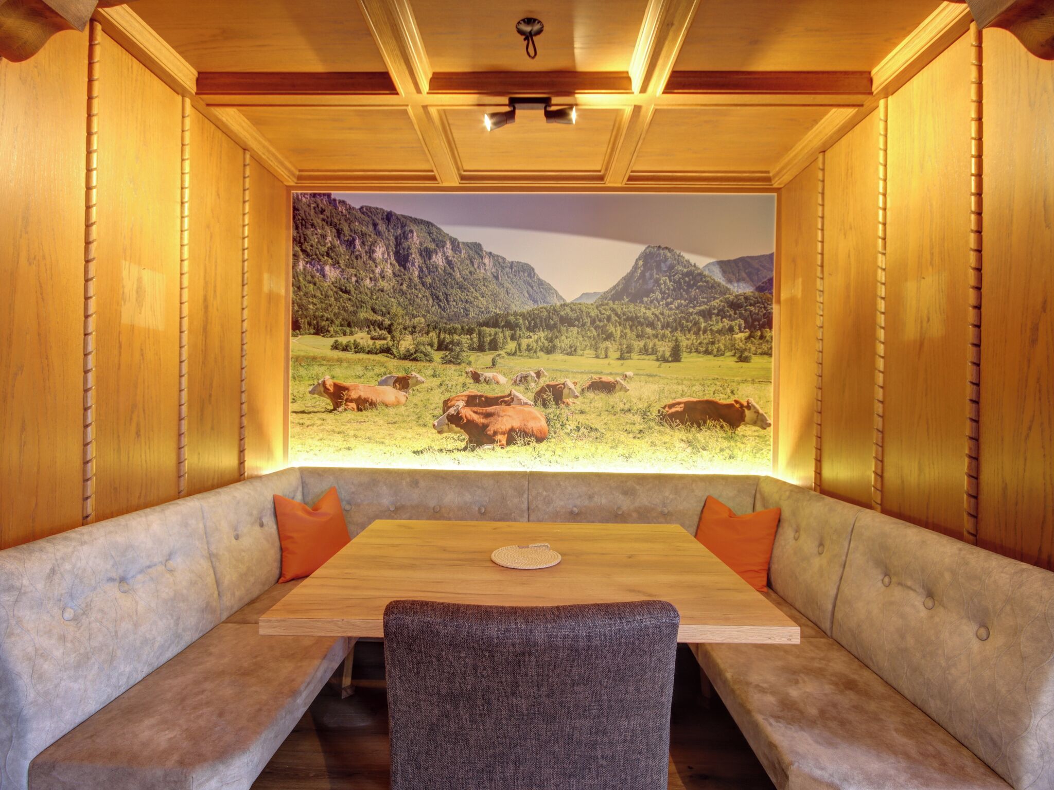 Un comedor con una mesa de madera y bancos acolchados, un mural grande de un paisaje montañoso, y paneles de madera en las paredes.