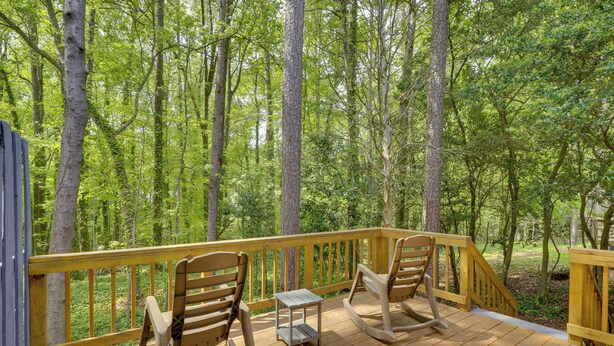 Una terraza de madera con dos mecedoras y una pequeña mesa, rodeada de un bosque.