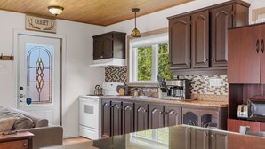 A kitchen with dark wooden cabinets, a white stove, and a window with a view of greenery. - Havre du Huit (Adstock)