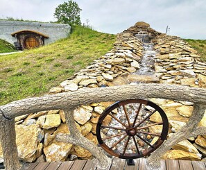 A stone water cascade with a wooden wheel in the foreground. - Restin' Holes Ky Bourbon Trail D -Sauna-HotTub-Gym-Playground-Waterfall-Themed (Willisburg)