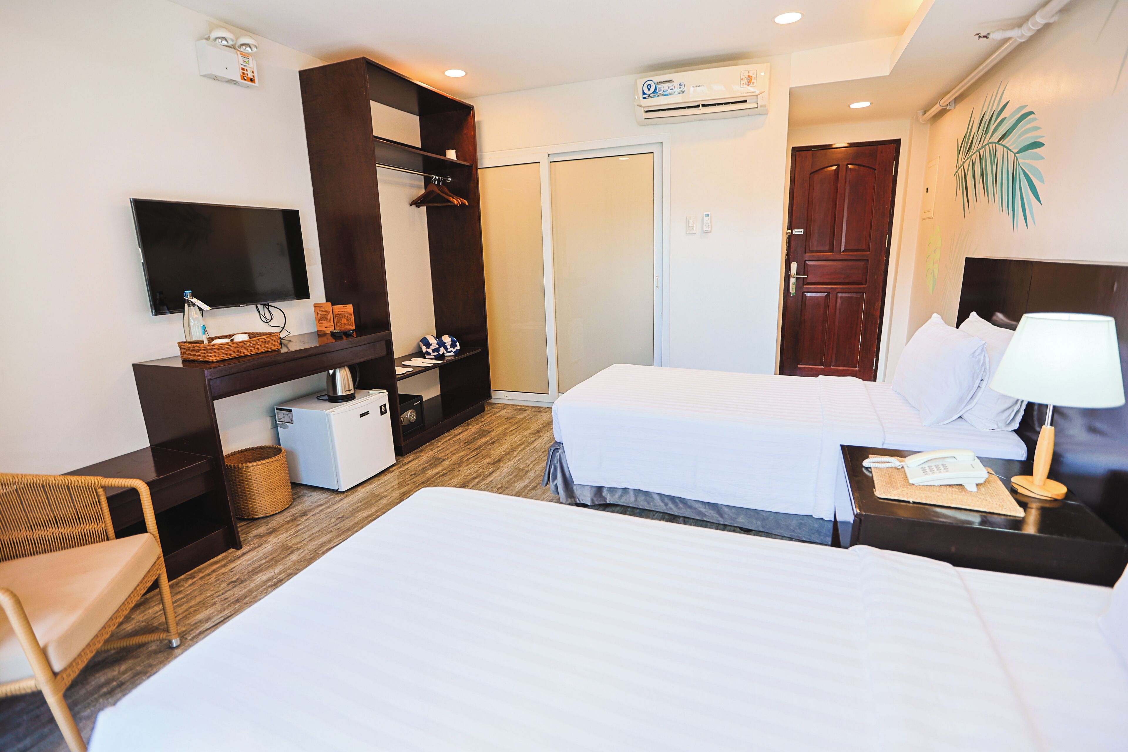 A hotel room with two beds, a TV, a desk with a computer, a wardrobe, and a door.