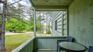 A porch with a table and chairs, overlooking a grassy area with trees and a road. - Indoor Pool, Hot Tub, Storyland (Bartlett)