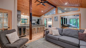 A modern interior with a wooden ceiling, a grey sofa, a bar area, and a kitchen. - Family-Friendly Chalet: Hot Tub, Games, Fire Pit (Jackson)
