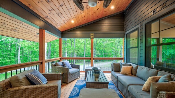 A covered porch with wicker furniture, a blue patterned rug, and a view of a forest. - Family-Friendly Chalet: Hot Tub, Games, Fire Pit (Jackson)