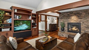 A spacious living room with a large flat-screen TV, leather sofas, a stone fireplace, and a wooden entertainment center.