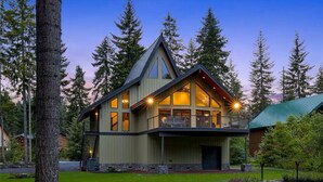 A modern two-story house with a large balcony, surrounded by tall trees.