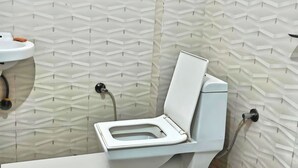 A modern bathroom with a white toilet, a sink, and a blue trash bin. - Prem Bhawan Guset House (Danta Ramgarh)