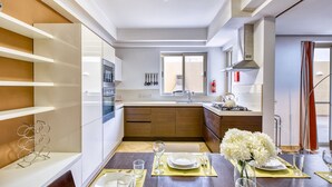 Eine moderne Küche mit weißen Schränken, einem eingebauten Backofen und einem Gasherd. Über der Spüle befindet sich ein Fenster, und es gibt eine Essecke mit einem Tisch für zwei Personen.