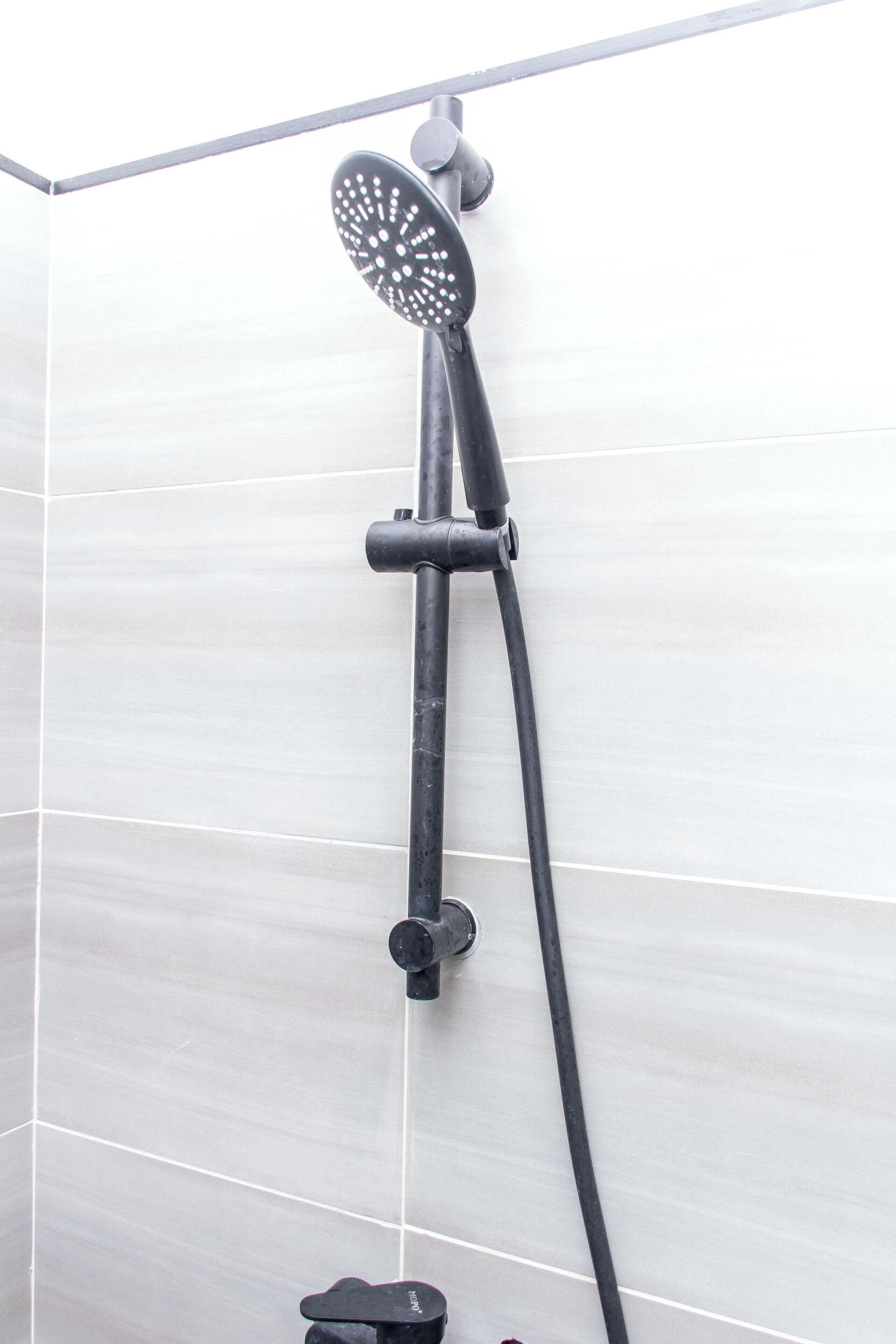 A shower with a handheld showerhead and a wall-mounted control valve.