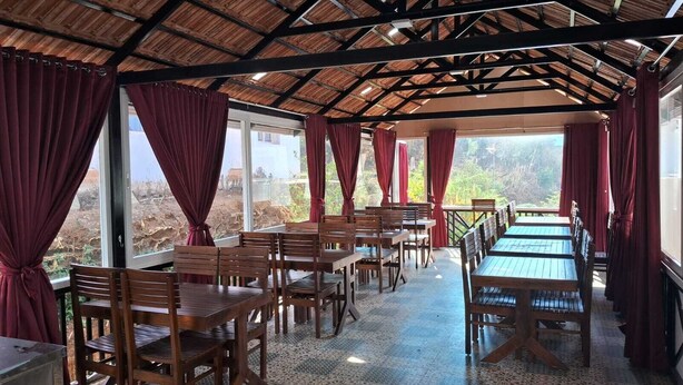 Een restaurant met houten tafels en stoelen, rode gordijnen en uitzicht op het buiten.