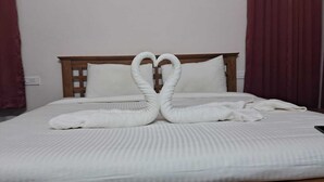 Een net opgemaakt bed met witte beddengoed en kussens, een houten hoofdbord en een handdoekje gevouwen in de vorm van een hart.