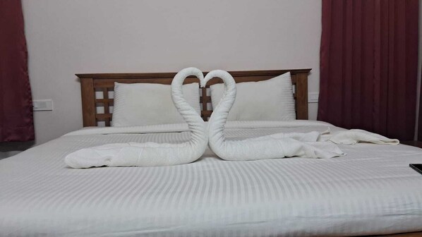 A neatly made bed with white bedding and pillows, a wooden headboard, and a heart-shaped towel arrangement. - Villa Bella (Ooty)