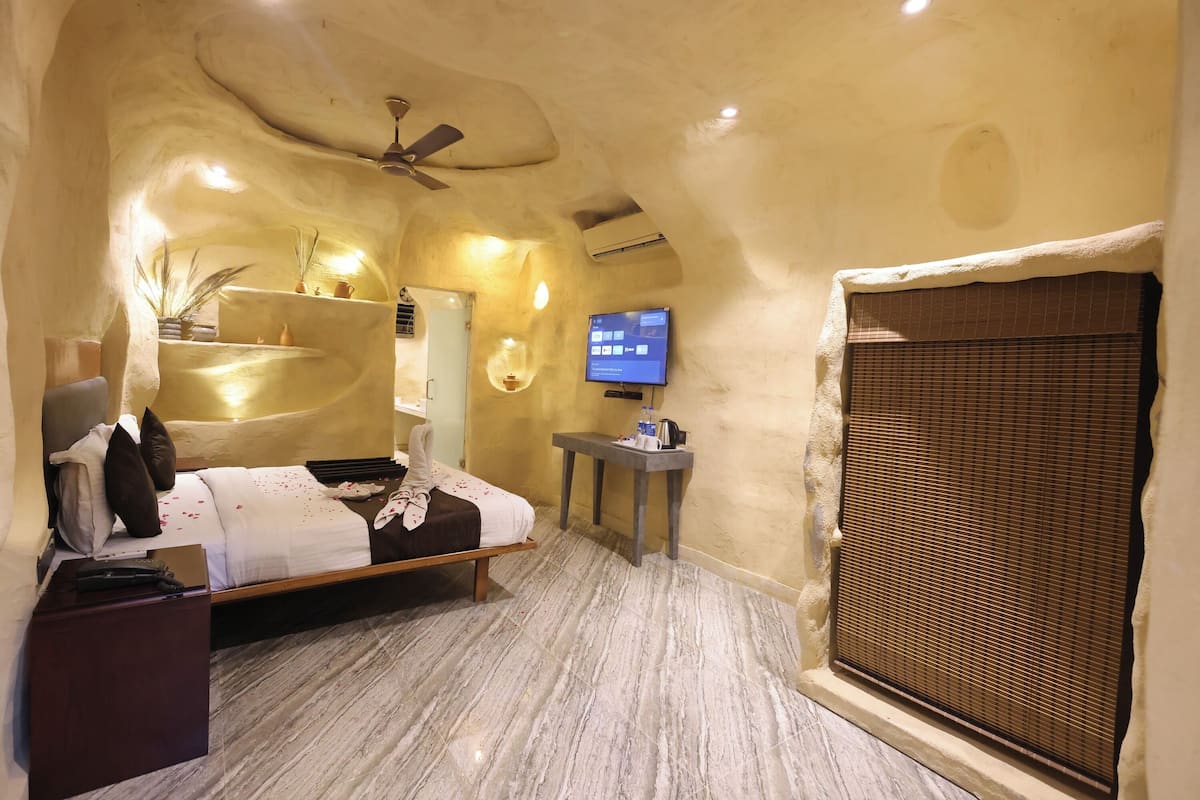 A bedroom with a bed, bedside table, TV, and a window with a blind.