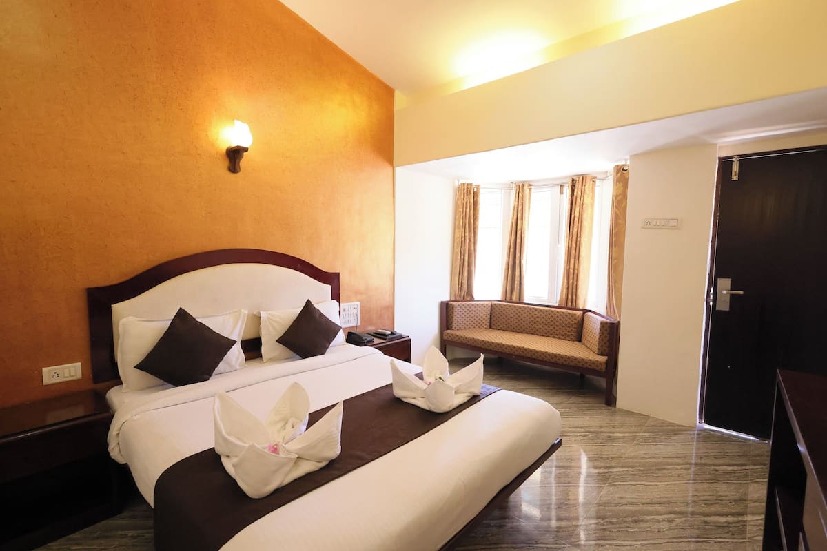 A hotel room with a large bed, a bedside table, a lamp, a sofa, and a door.