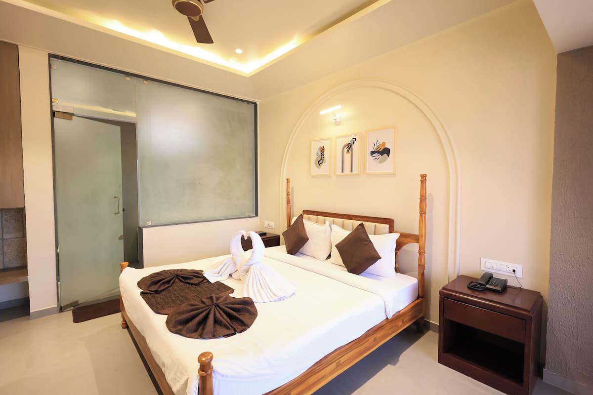 A hotel room with a large bed, a bedside table with a phone, and a glass door leading to a shower area.
