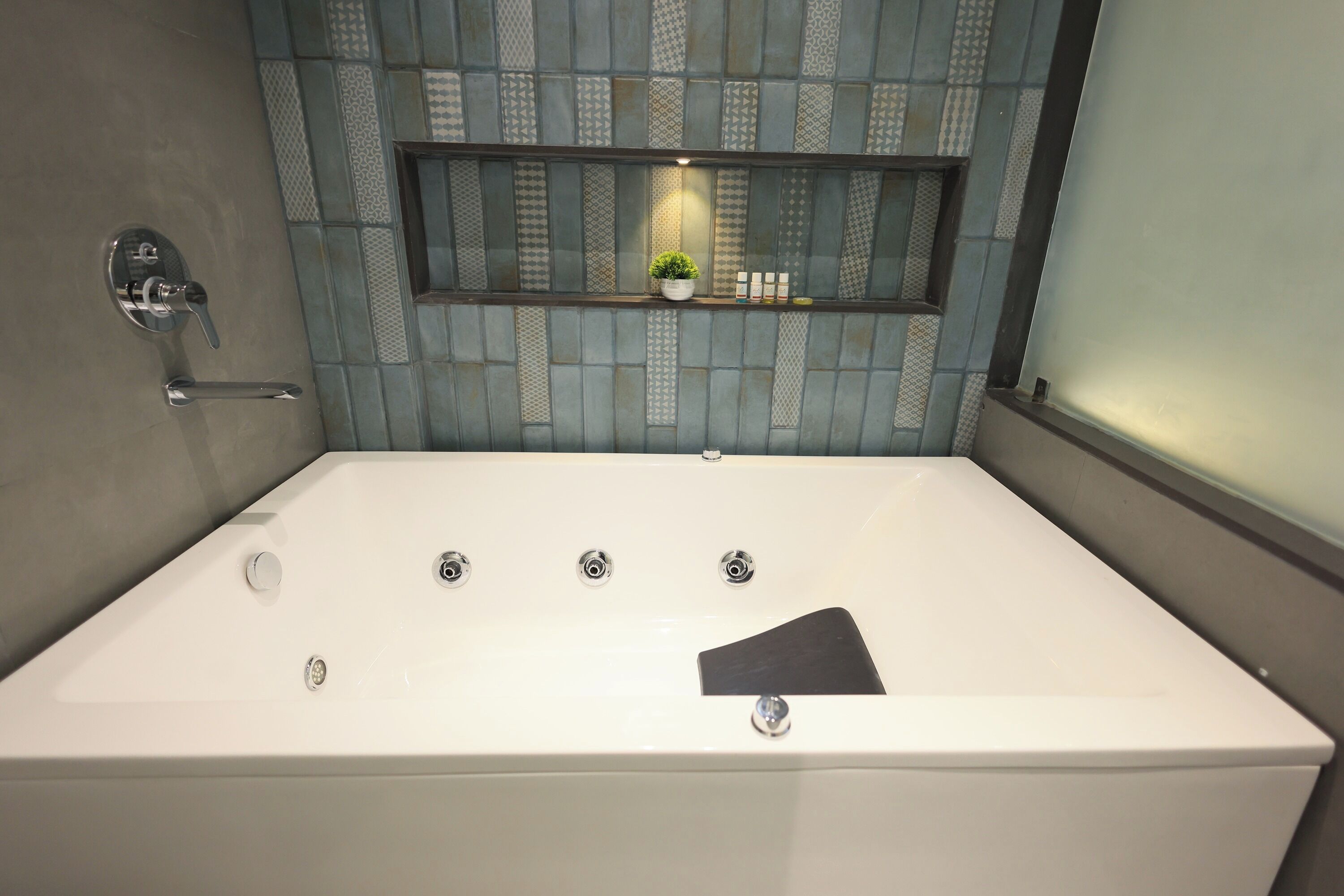 A modern bathroom with a large bathtub, a built-in shelf with toiletries, and a potted plant.