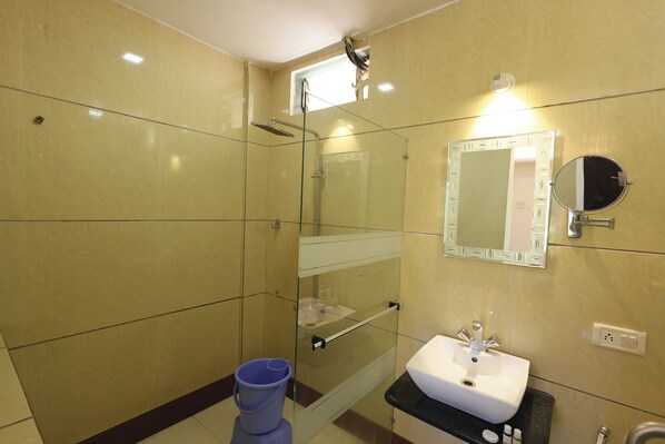 A bathroom with a glass shower enclosure, a sink with a mirror, and a blue bucket.