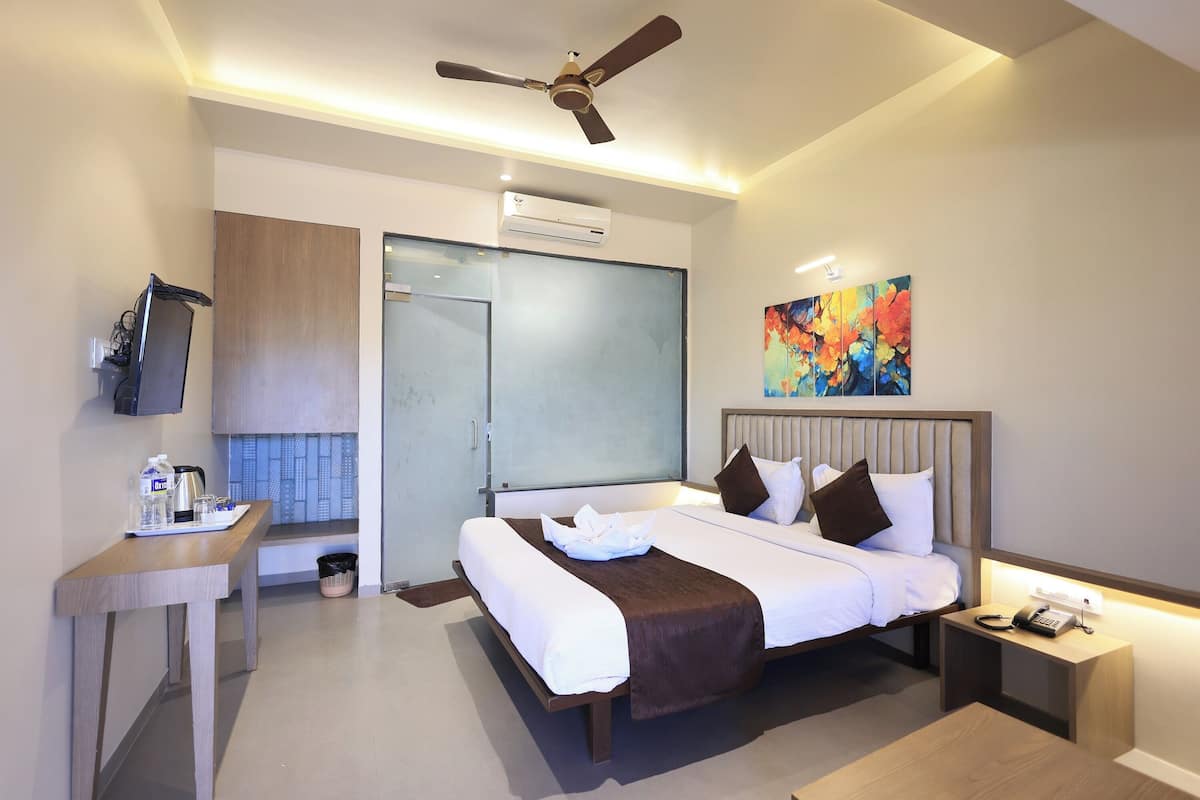 A modern hotel room with a large bed, a desk with a flat-screen TV, a ceiling fan, and a colorful abstract painting.