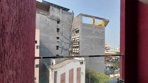 A balcony with a view of a building under construction, featuring a glass railing and a red wall. - V & U Homestay Sadar (Nagpur)