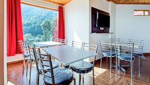 Un comedor con mesa y sillas, un televisor de pantalla plana en la pared, y vistas al bosque a través de amplios ventanales.