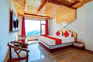 A bedroom with a wooden ceiling, a bed with red and white bedding, a TV mounted on the wall, and a window with a view of the mountains. - Shree Namah Residency (Shimla)