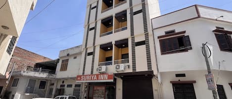 A multi-story building with a sign for 'Suriya Inn' indicating it is a hotel. There are parked vehicles and motorcycles in front, and the building has multiple balconies.
