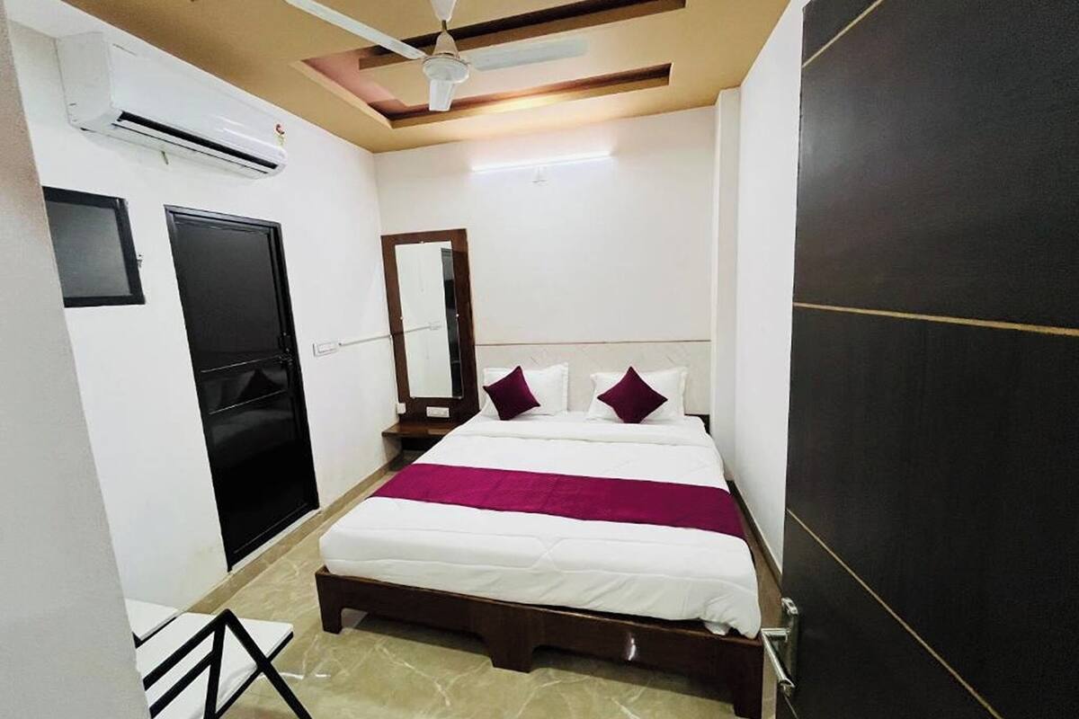 A bedroom with a bed, a ceiling fan, an air conditioning unit, a door, and a mirror.