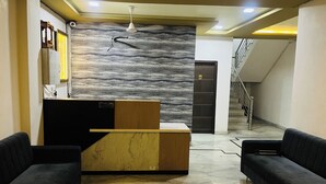 A reception area with a marble wall, a wooden reception desk, two black sofas, and a staircase in the background. - Suriya Inn (Udaipur)