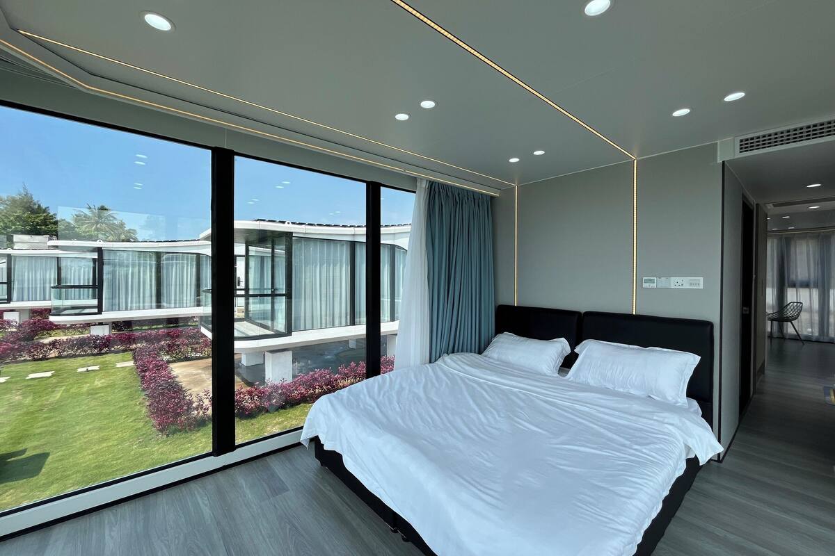 A modern hotel room with a large bed, a view of the garden, and a balcony.