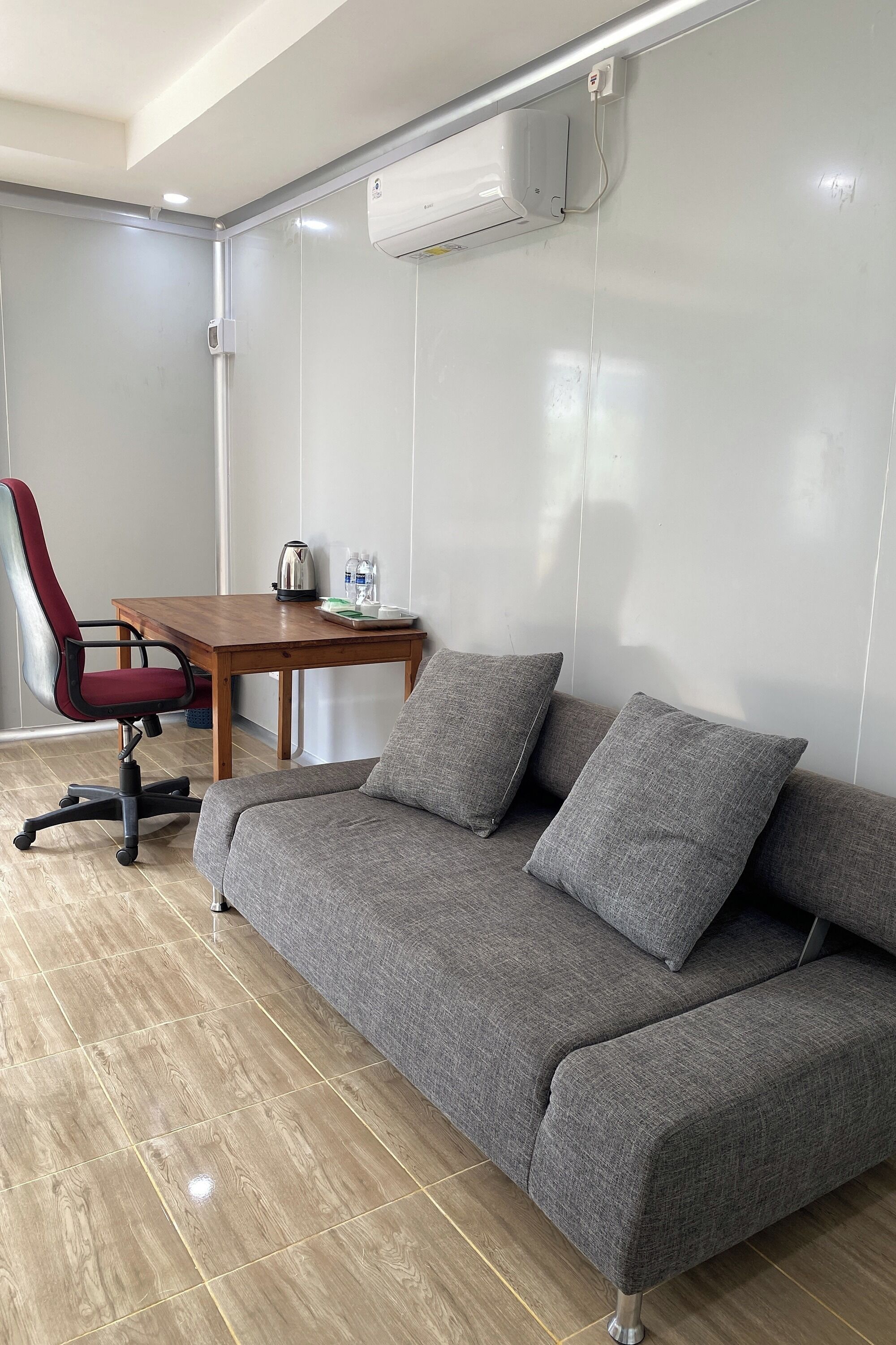 A modern room with a grey sofa, a wooden table with a kettle, and a red office chair.