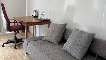 A modern room with a grey sofa, a wooden table with a kettle, and a red office chair.