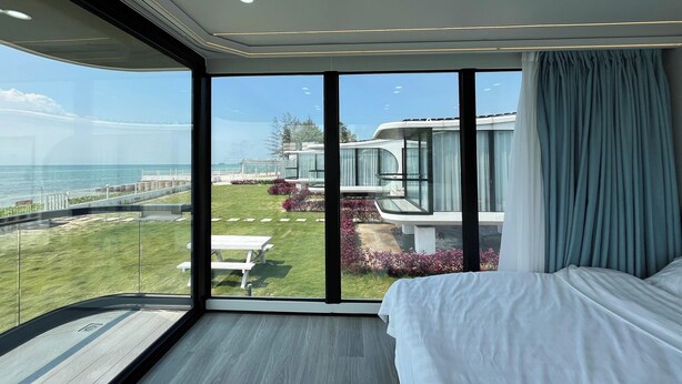 Ein modernes Hotelzimmer mit großem Balkon, einem Bett und Blick auf das Meer und den Garten.