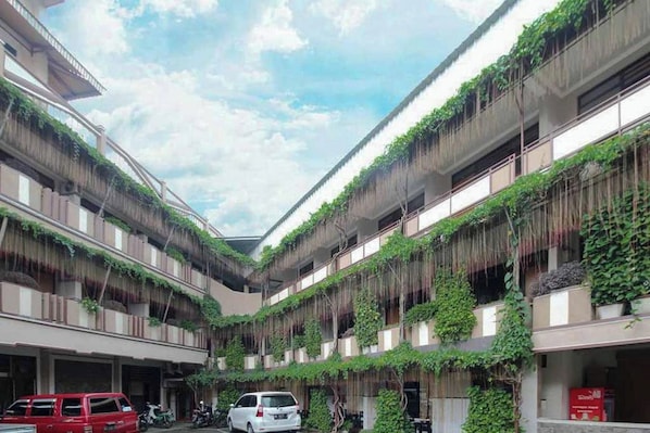 Un edificio de varios pisos con balcones cubiertos de follaje, un patio central con vehículos estacionados y un cielo despejado.