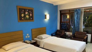 Ein Hotelzimmer mit zwei Betten, einem Schreibtisch mit Stuhl, einem Telefon und einem Fenster mit Vorhängen.