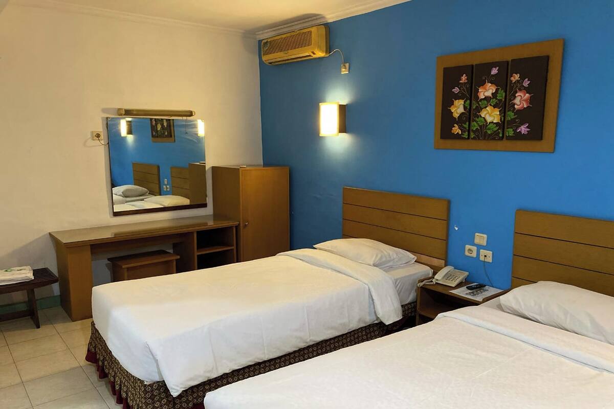 A hotel room with two beds, a desk, a mirror, a wall-mounted air conditioner, and a bedside telephone.