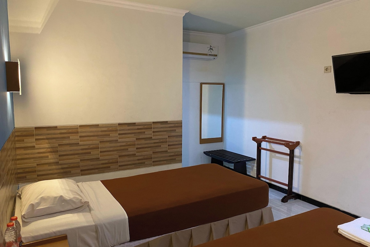 A hotel room with two beds, a wooden headboard, a flat-screen TV, a mirror, and a small table.