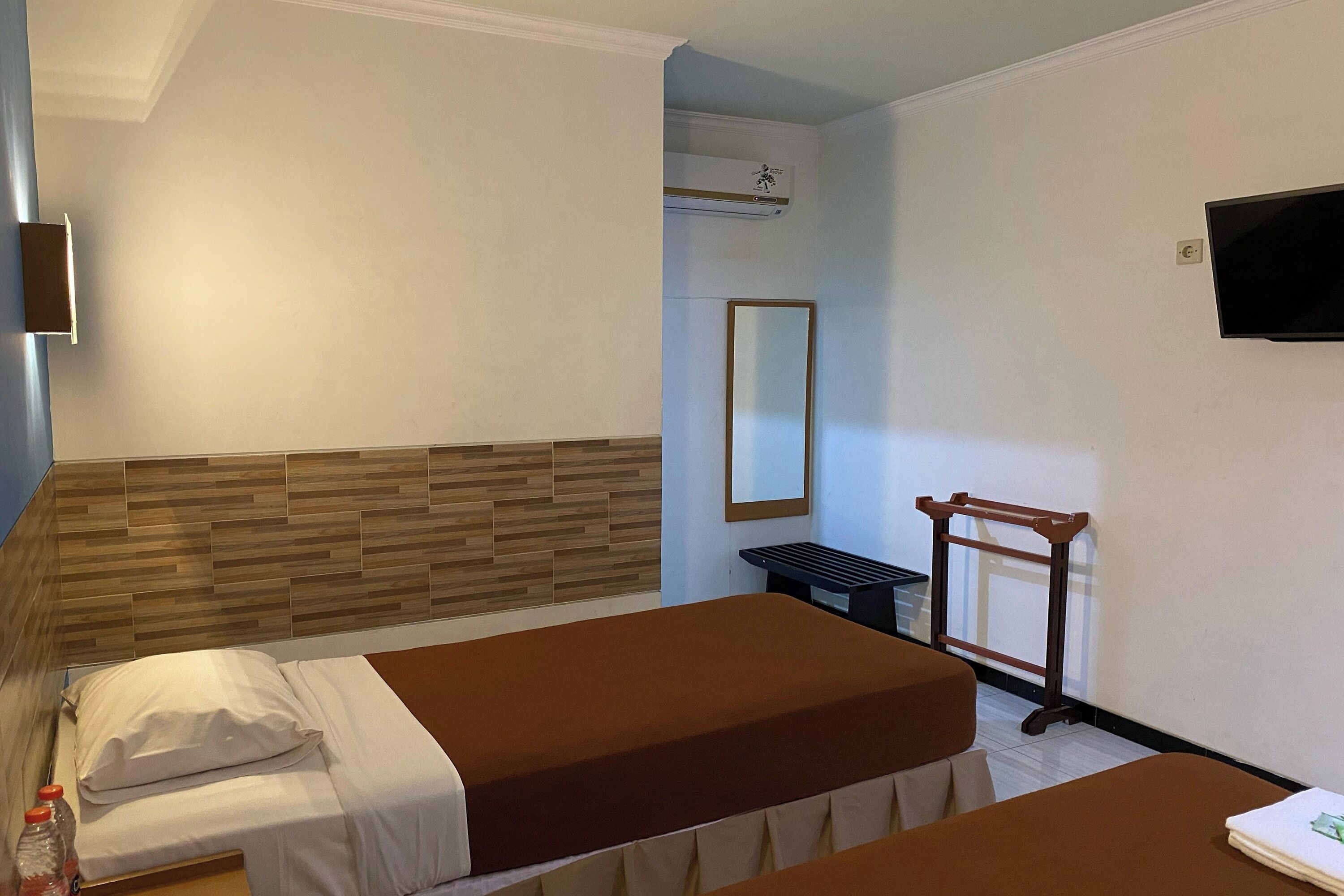 A hotel room with two beds, a wooden headboard, a flat-screen TV, a mirror, and a small table.