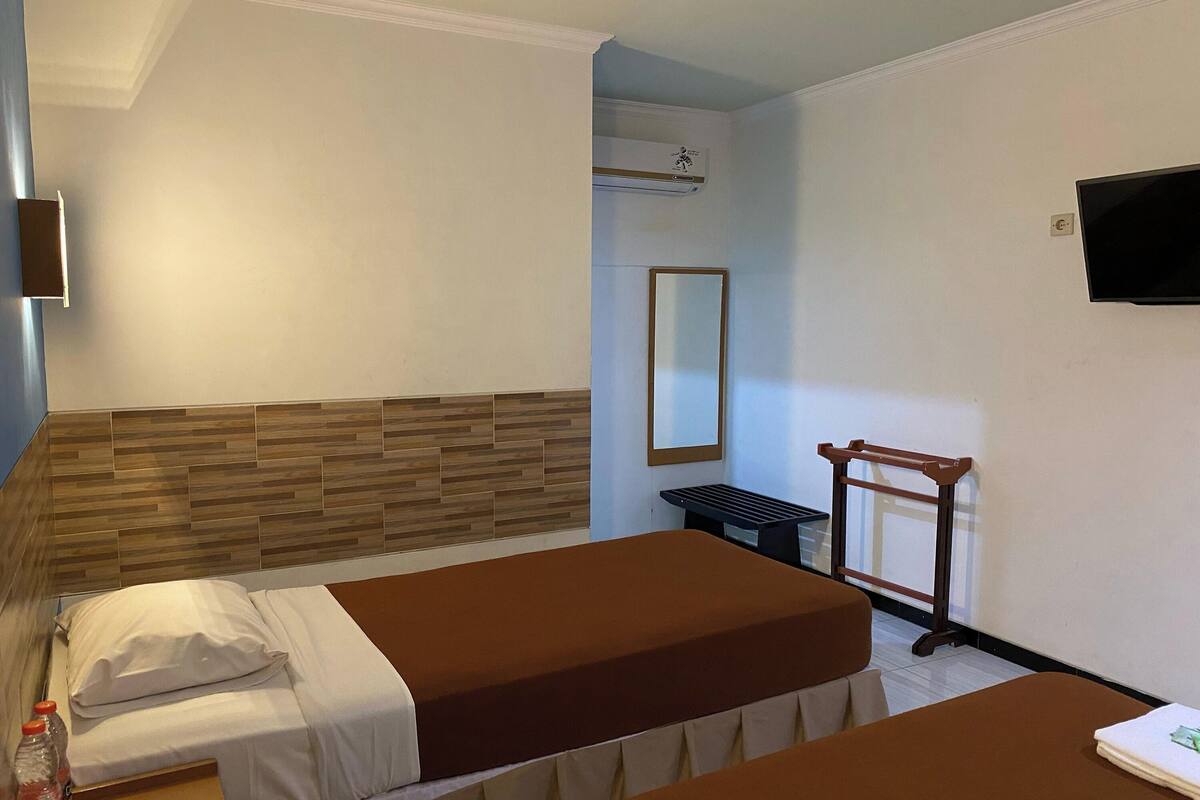 A hotel room with two beds, a wooden headboard, a flat-screen TV, a mirror, and a small table.