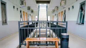 A corridor with a central staircase, a wooden bench, and a trash bin. - Griya Safitri Syariah (Palembang)