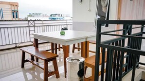 A room with a white table, wooden benches, a trash can, and a view of buildings through a window. - Griya Safitri Syariah (Palembang)