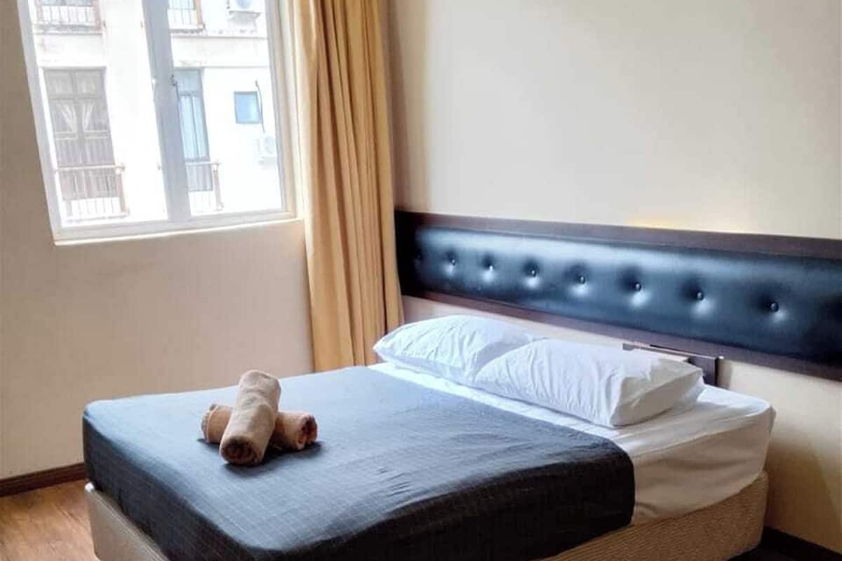 A neatly made bed with a dark mattress and white pillows, a wooden floor, a window with curtains, and a painting on the wall.