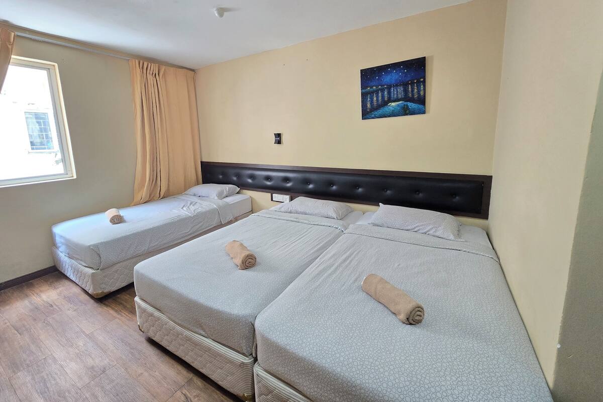 A hotel room with two beds, a window with curtains, a night sky painting on the wall, and a ceiling light.