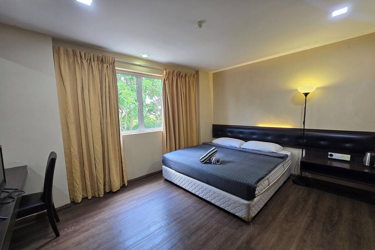 A bedroom with a bed, a desk, a chair, a window with curtains, and a bedside lamp.