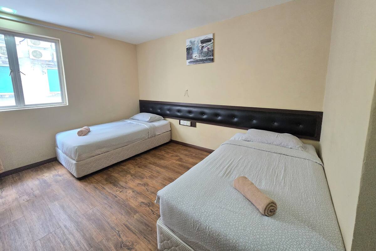 A small, clean room with two single beds, a window, and a wall-mounted picture.