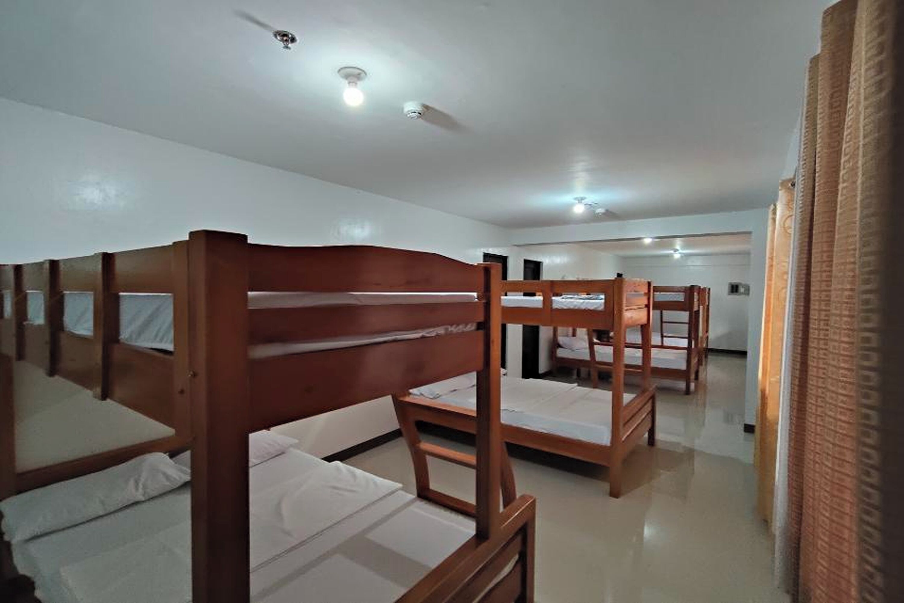 Una habitación de hotel con literas, ventilador de techo y baño a la vista.