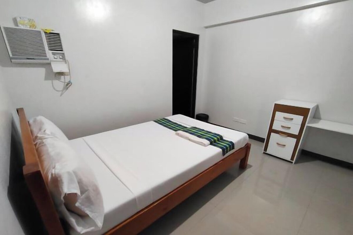 A bedroom with a bed, a bedside table, a wardrobe, and an air conditioning unit.
