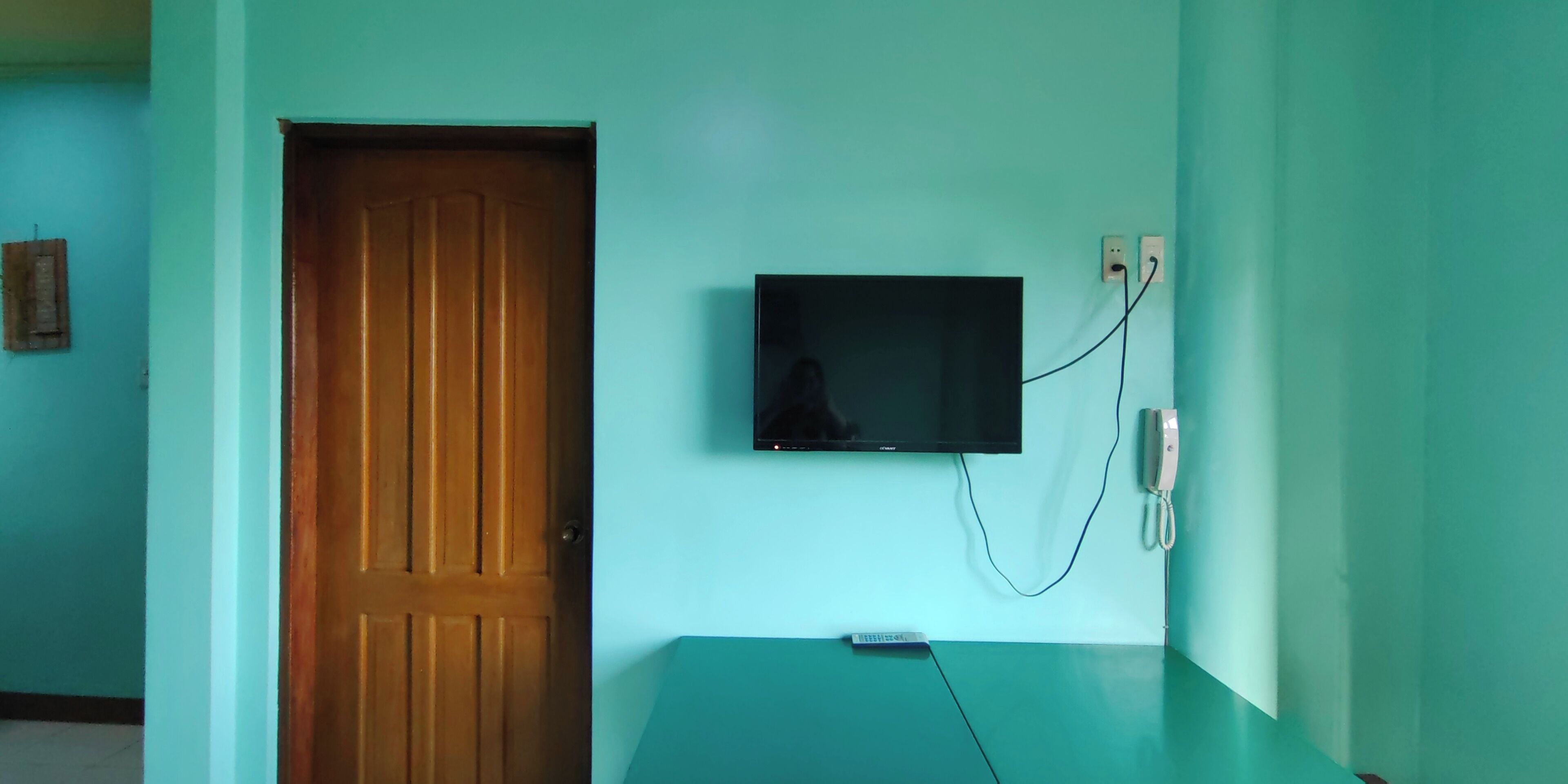 A room with a wooden door, a flat-screen TV mounted on the wall, and a remote control on the floor.