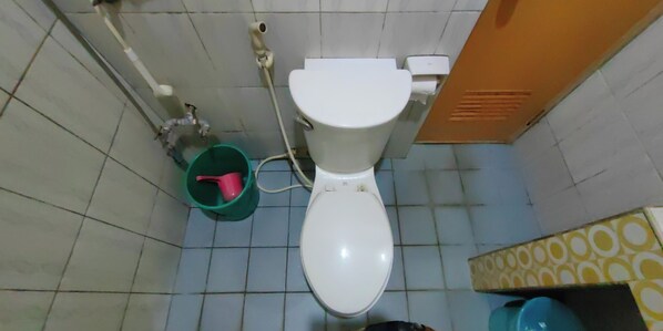 Un baño con un inodoro blanco, un cubo verde y una pared amarilla con estampado.
