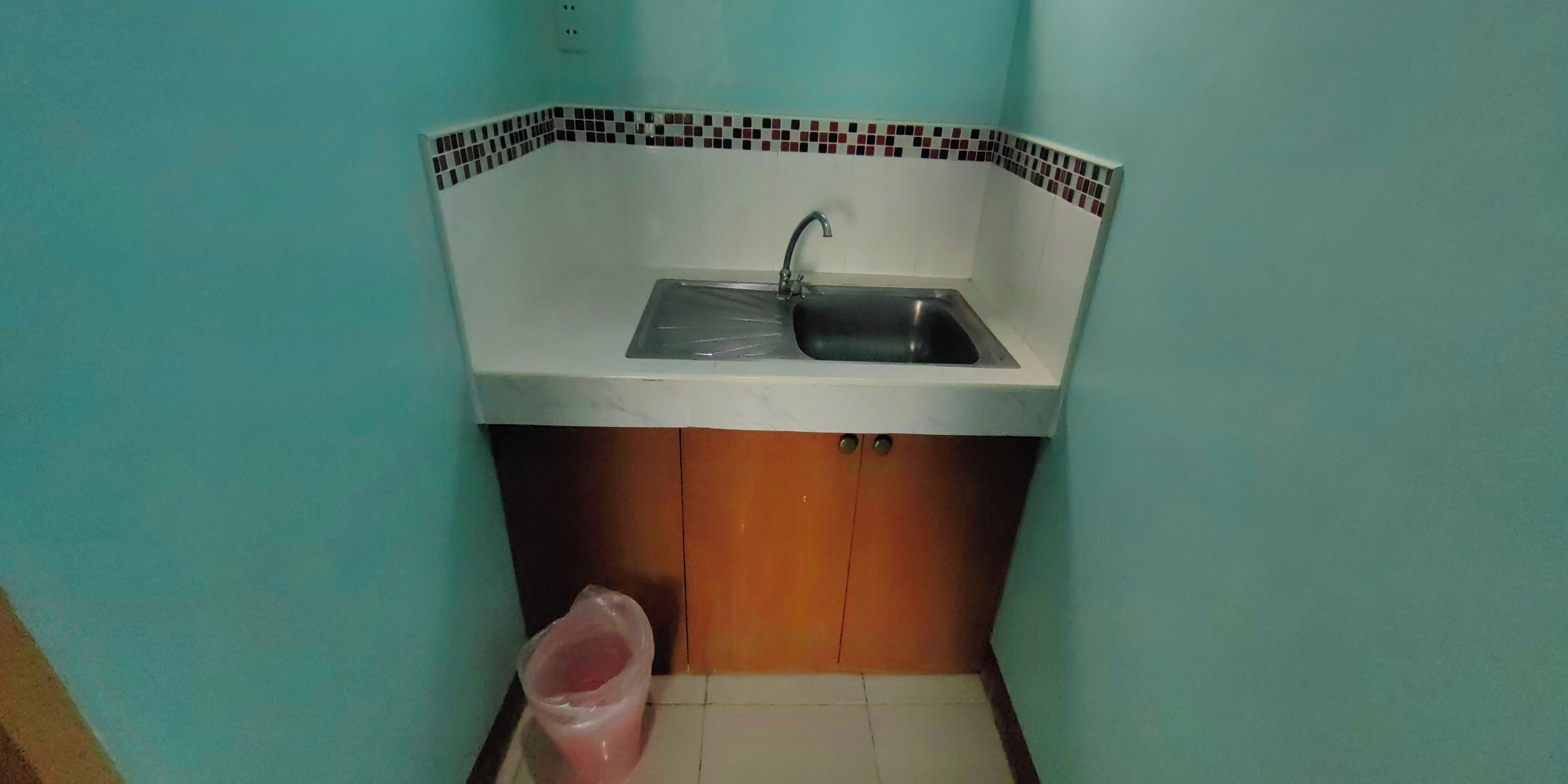 A small kitchen with a sink, a trash bin, and a tiled backsplash.
