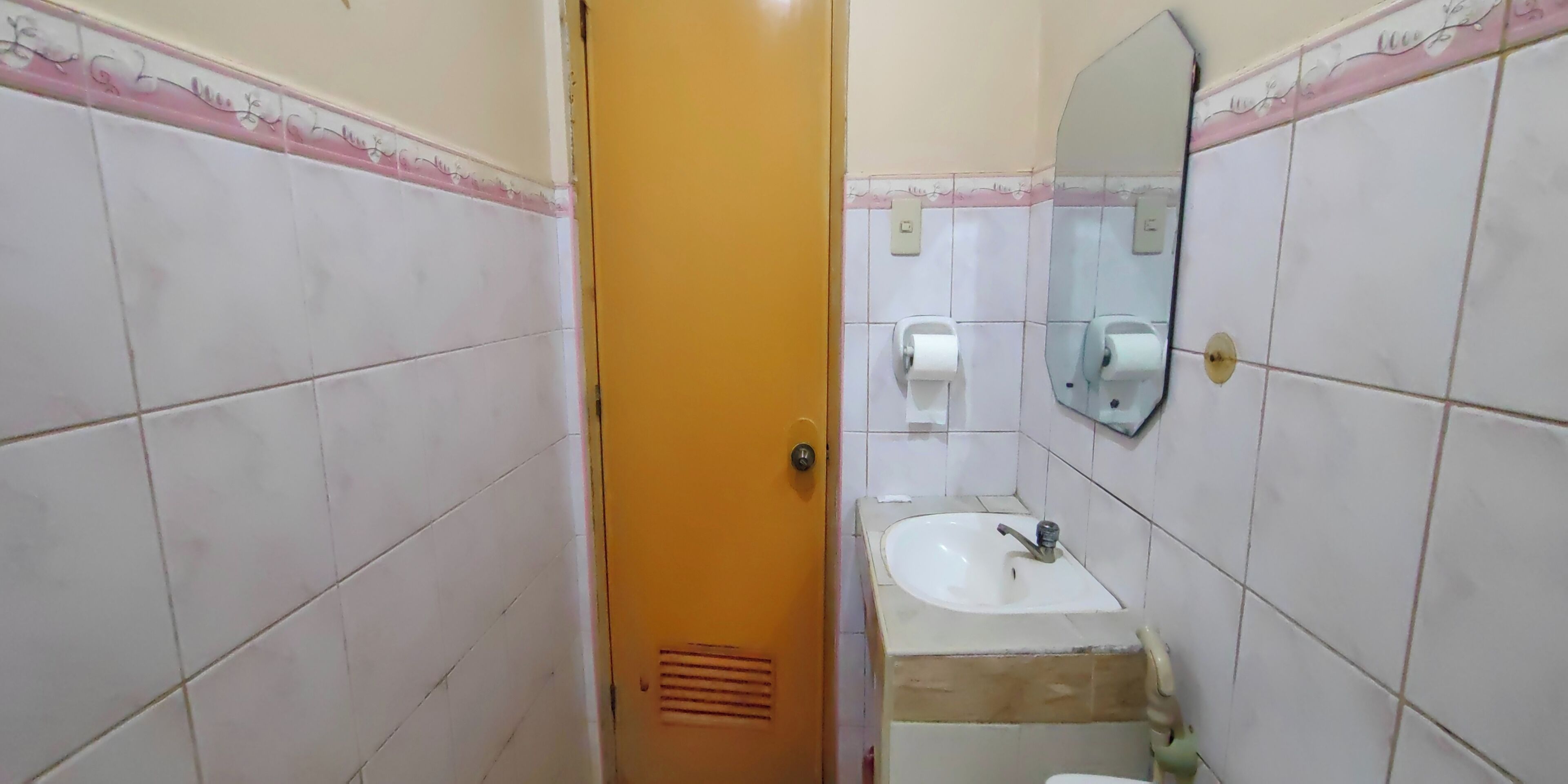 A bathroom with white tiled walls, a sink with a mirror above it, and a door with a handle.